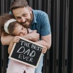 Father and daughter embrace with a sign saying 'The Best Dad Ever.'