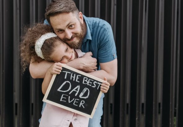 Father and daughter embrace with a sign saying 'The Best Dad Ever.'